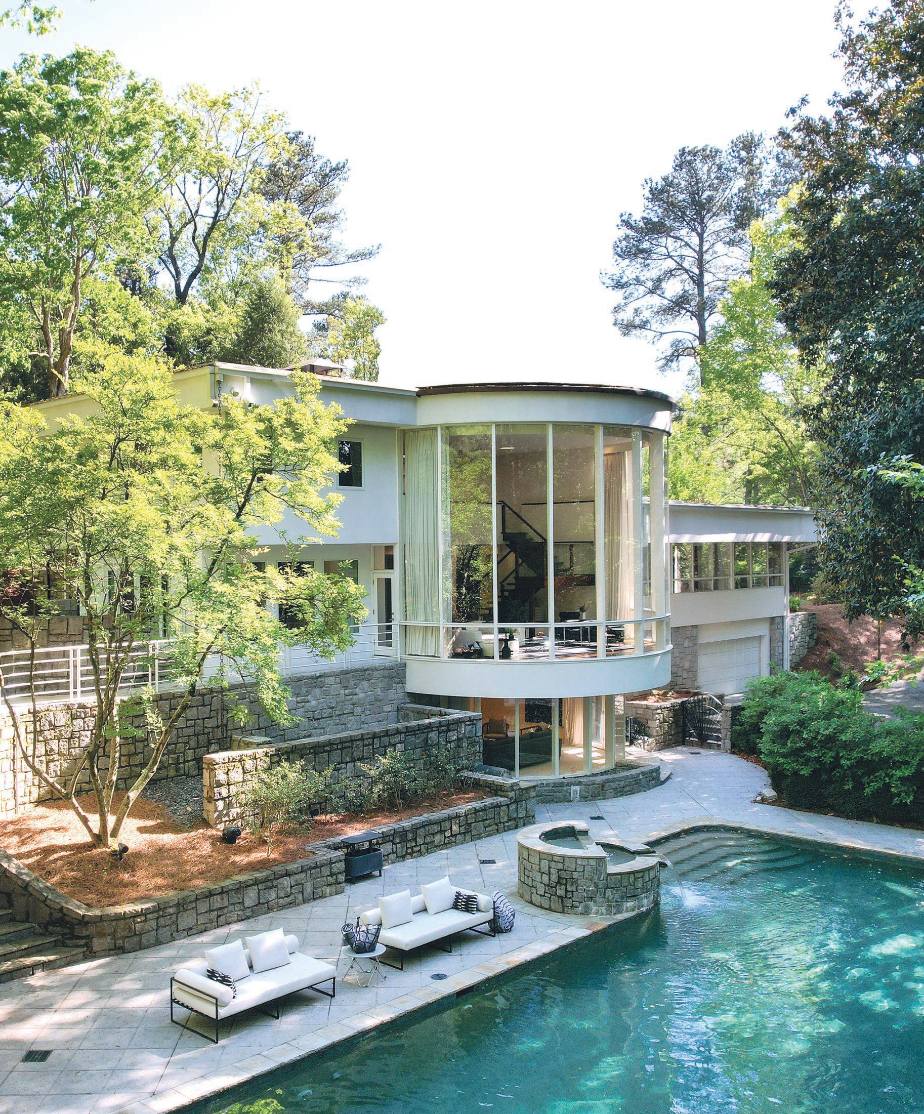 A view of the back of the house that features captivating floor-to-ceiling curved glass walls that overlook the large pebble tec pool. PHOTO COURTESY OF BERKSHIRE HATHAWAY HOMESERVICE GA PROPERTIES